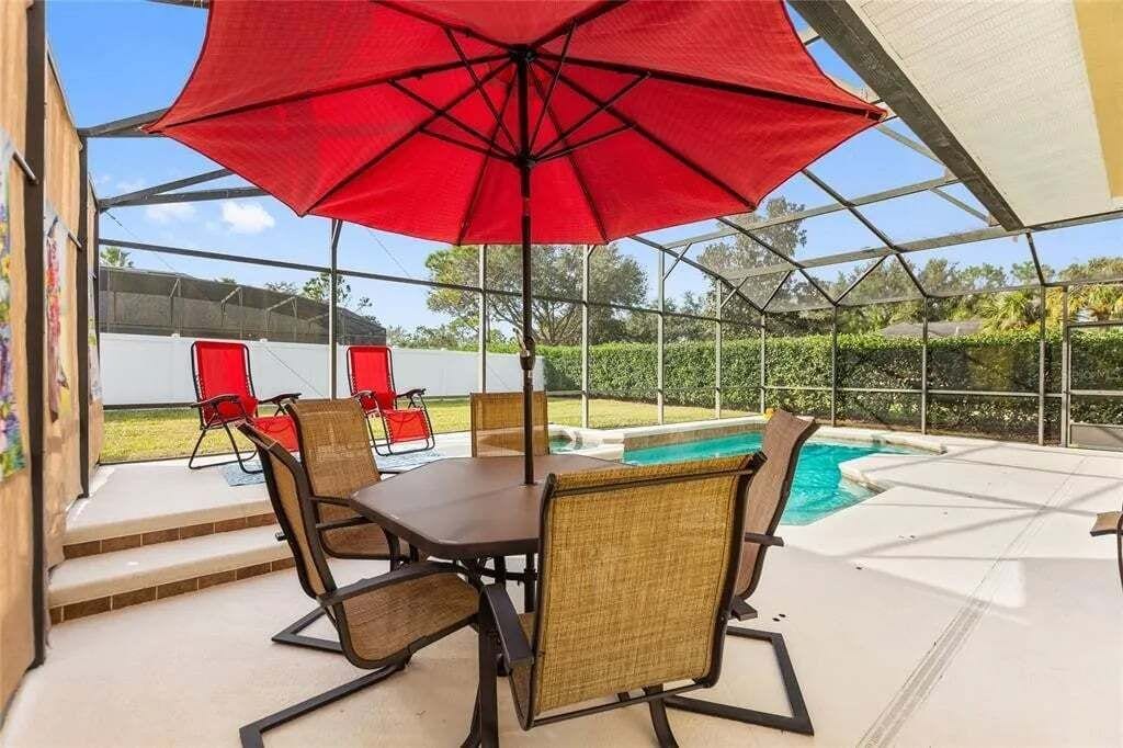 Eine überdachte Terrasse im Freien mit Tisch, Stühlen, einem roten Sonnenschirm und einem Pool.
