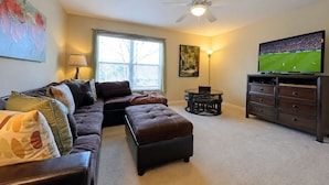 A living room with a sofa, ottoman, TV, ceiling fan, and artwork on the walls. - 6BR Private Pool Home at West Haven Gated Community (Davenport)