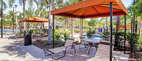 Un espace extérieur aménagé en terrasse, avec des bancs, des tables et des parasols en bois offrant de l’ombre.
