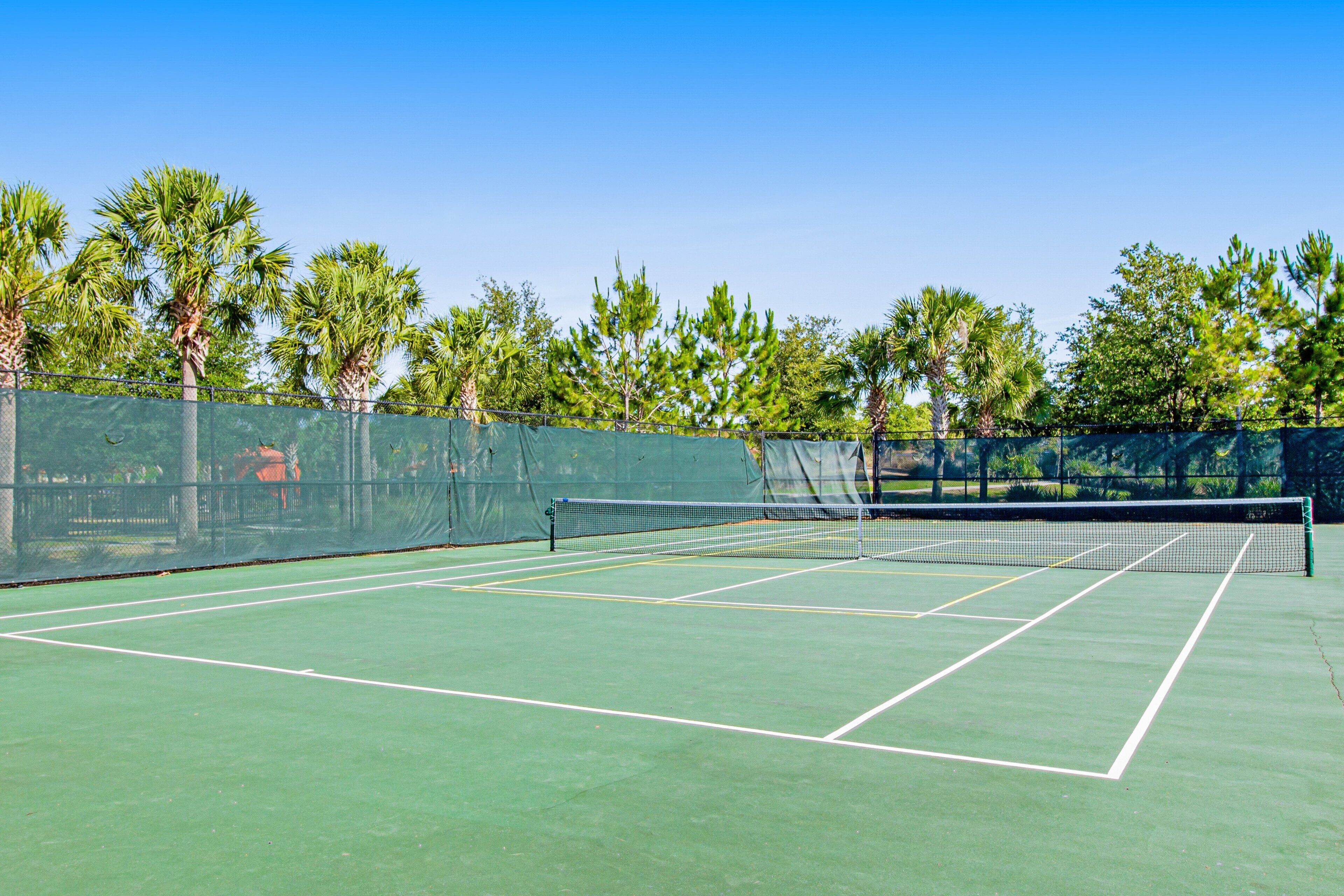A tennis court with a net, surrounded by trees and a fence.