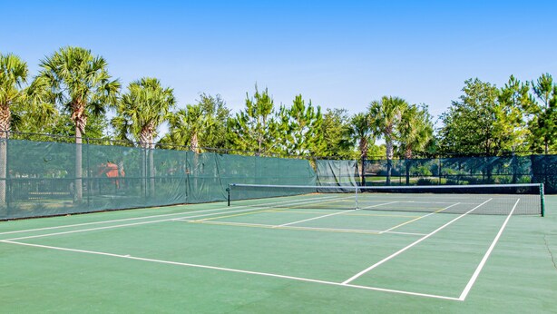 Ein Tennisplatz mit Netz, umgeben von Bäumen und einem Zaun.