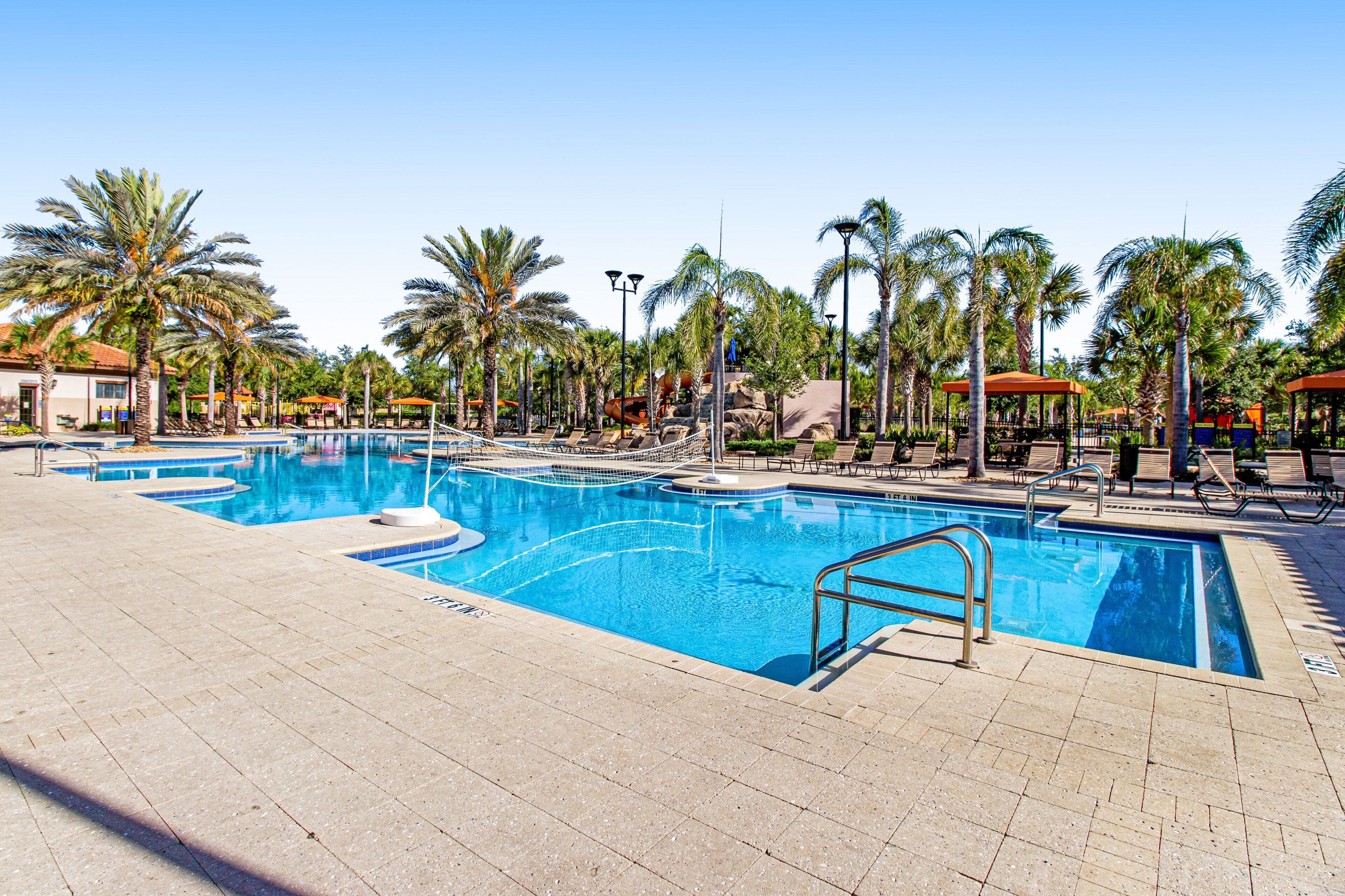 A swimming pool with a diving board, surrounded by palm trees and lounge chairs.