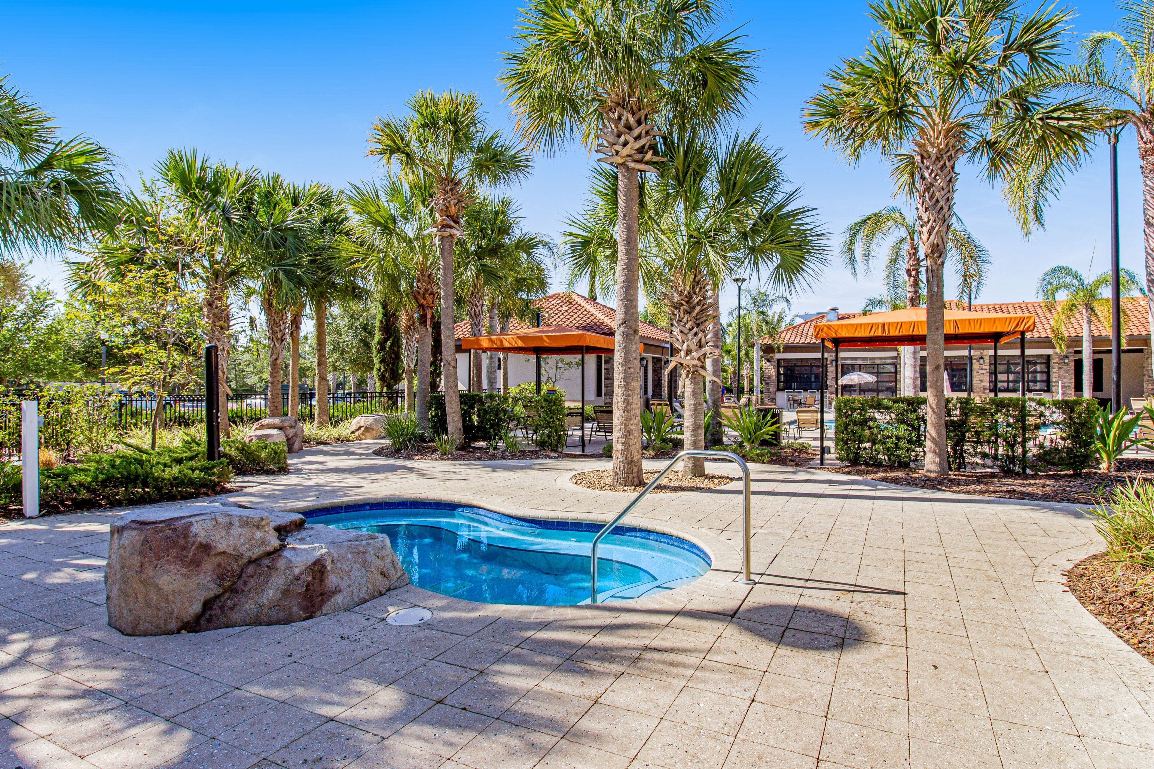 A pool area with a curved pool, surrounded by palm trees and a building with a tiled roof.