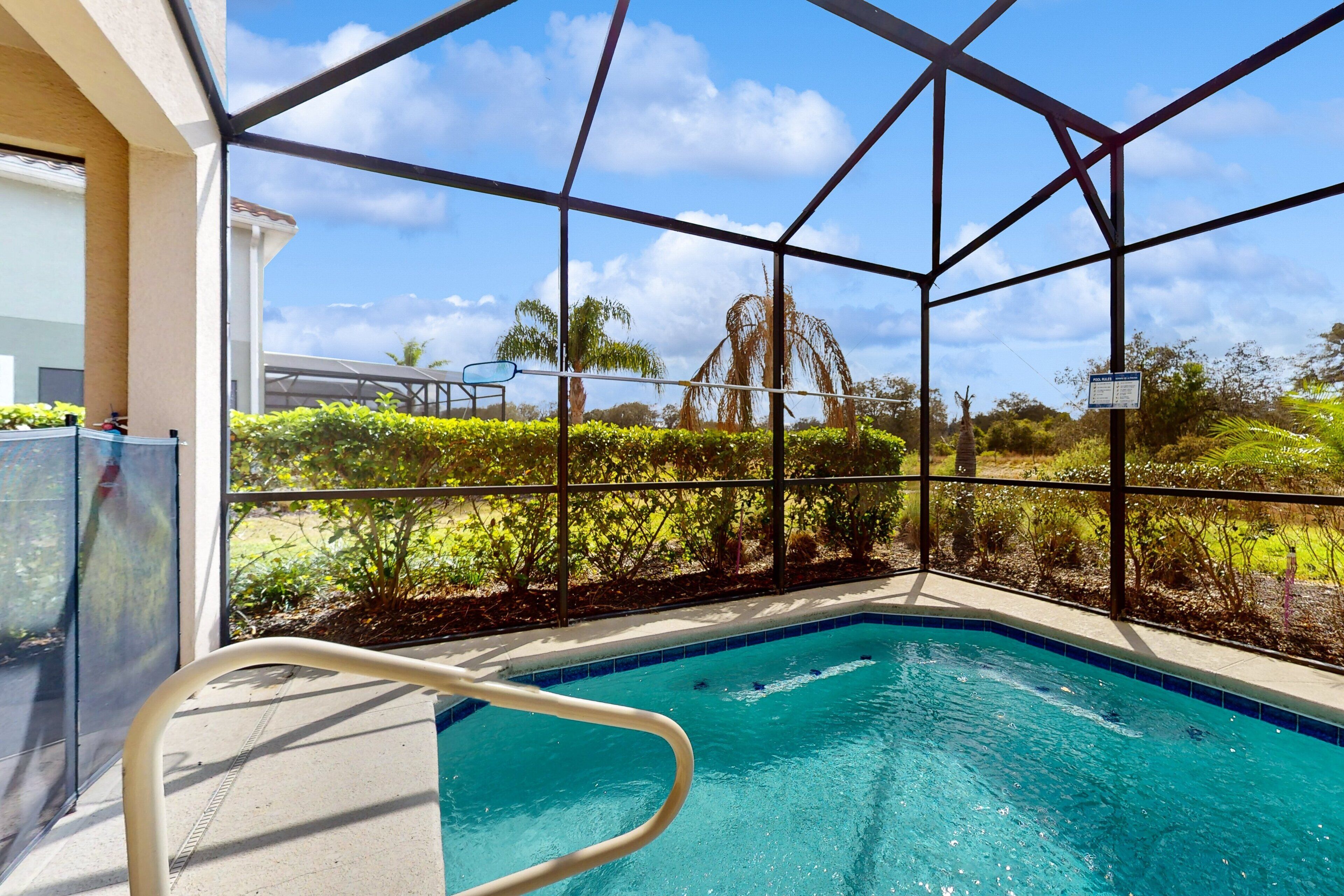 A pool with clear blue water, surrounded by a glass enclosure with a view of greenery and a palm tree.