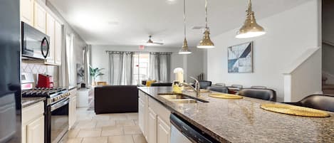 A modern kitchen with granite countertops, stainless steel appliances, and pendant lighting.