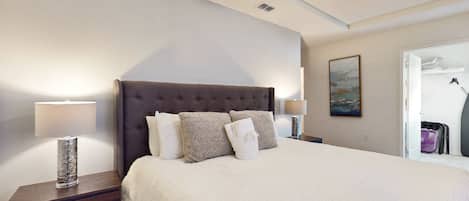 A hotel room with a large bed, two bedside tables, a ceiling fan, and a painting on the wall.