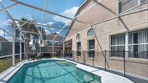 Uma piscina com superfície de água azul translúcida, rodeada por um terraço coberto com cadeiras e uma mesa.