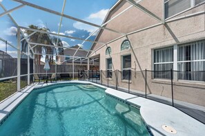 A swimming pool with a clear blue water surface, surrounded by a covered patio area with chairs and a table. - Golden Light Retreat-spacious 5BR Pool Home Near Disney (Davenport)
