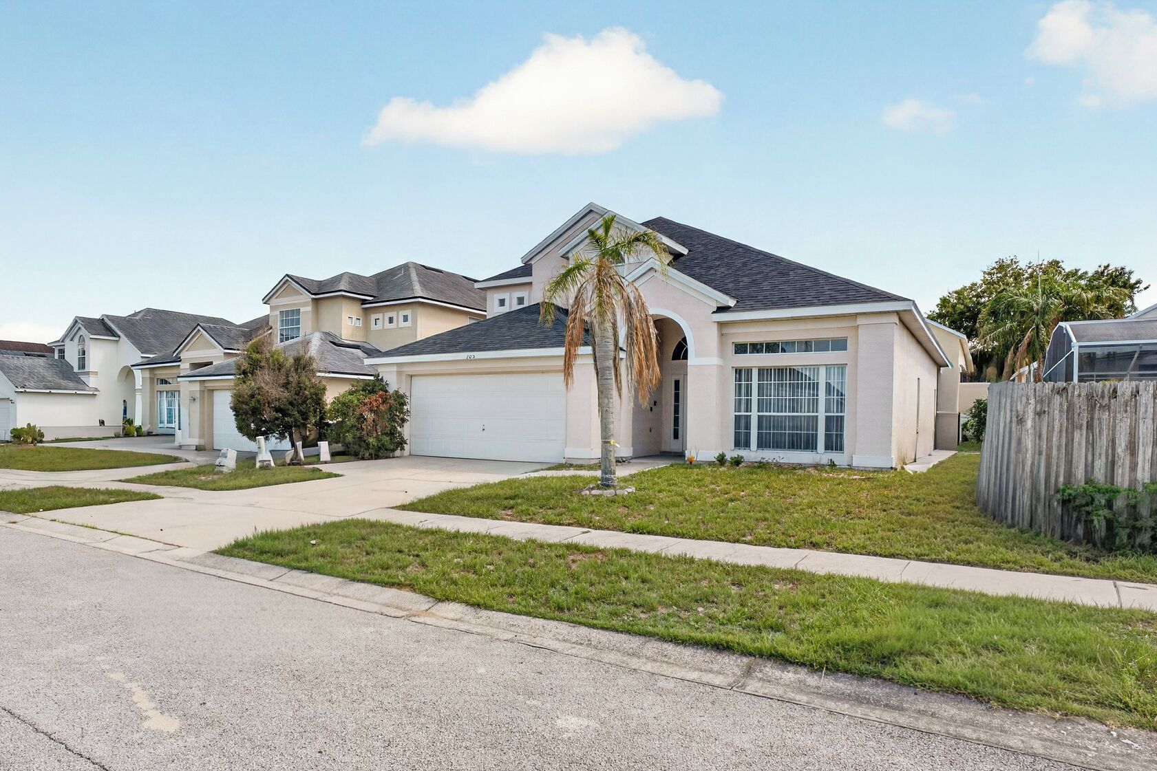 A residential area with single-family homes featuring front yards, driveways, and a clear sky.
