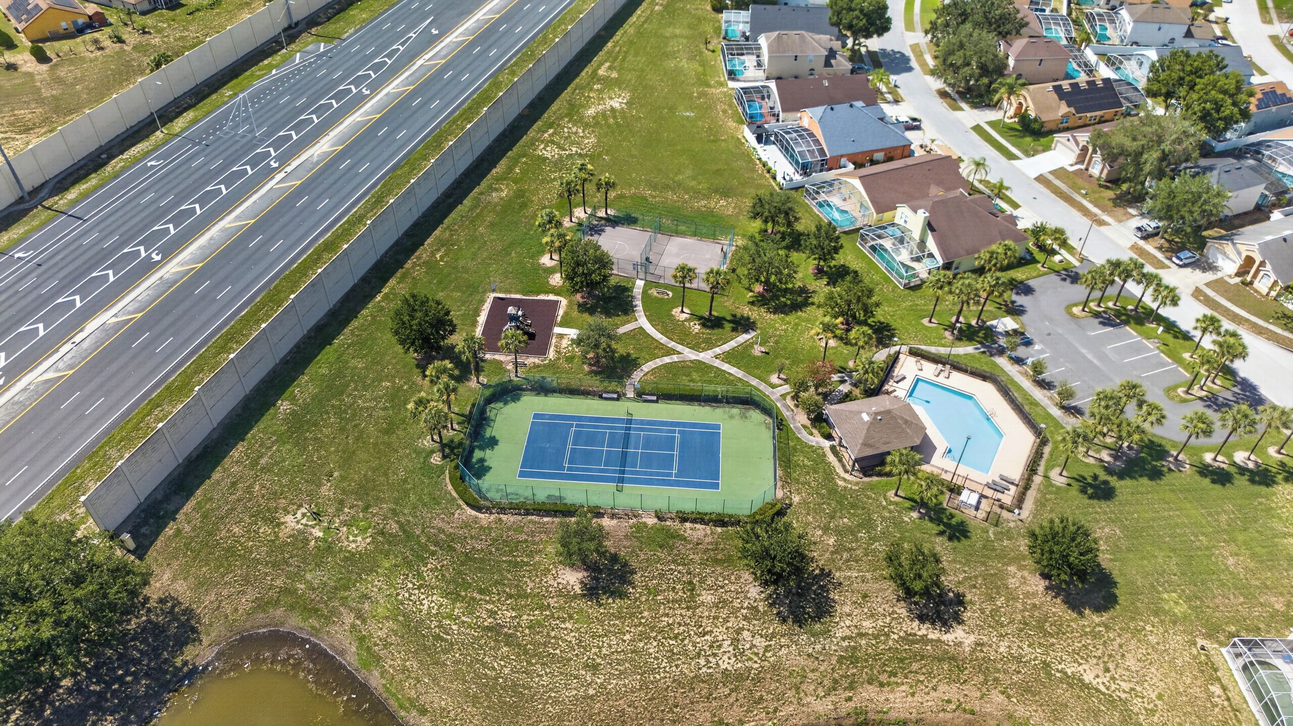 An aerial view of a residential area with a tennis court, a swimming pool, and a road with a median.