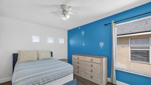 Quarto com cama, penteadeira e janela com persianas.