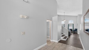 Um interior moderno com uma escada que leva a uma sala de jantar, paredes cinza claro e piso de madeira.
