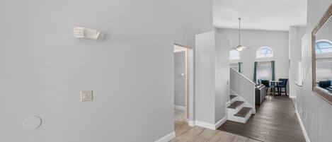 Um interior moderno com uma escada que leva a uma sala de jantar, paredes cinza claro e piso de madeira.