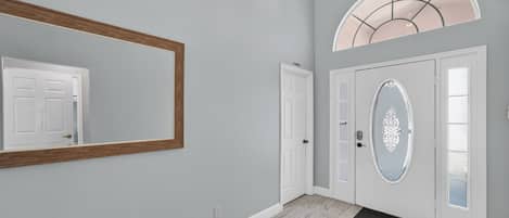 A hallway with a large mirror, a door with a decorative glass panel, and a light fixture above.