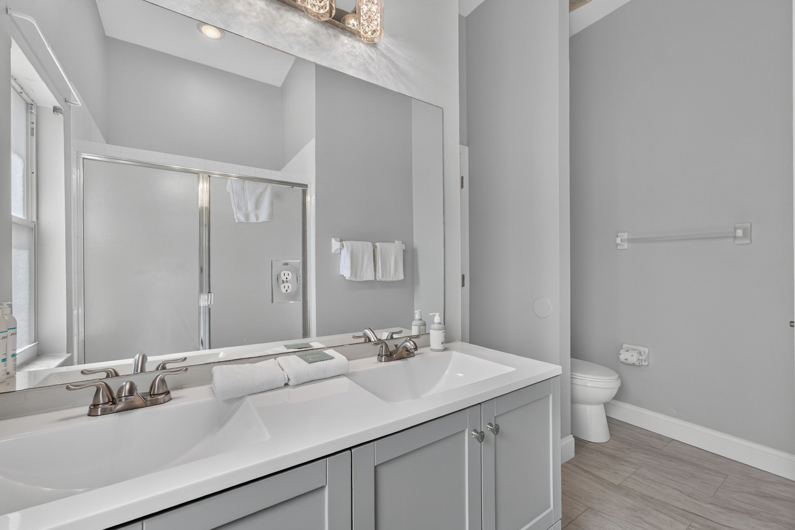 A modern bathroom with a large mirror, two sinks, and a shower.