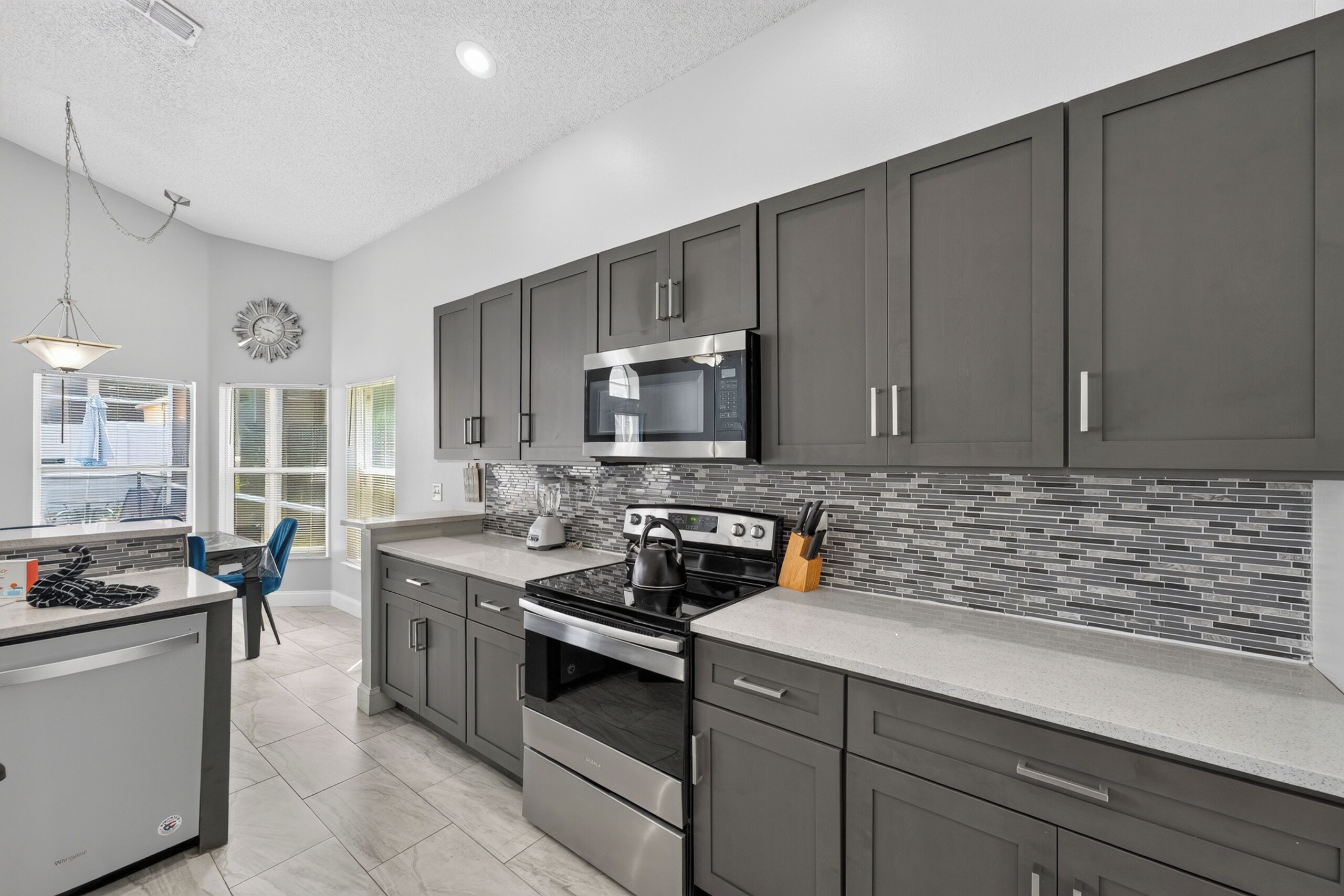 A modern kitchen with grey cabinets, stainless steel appliances, and a tiled backsplash.