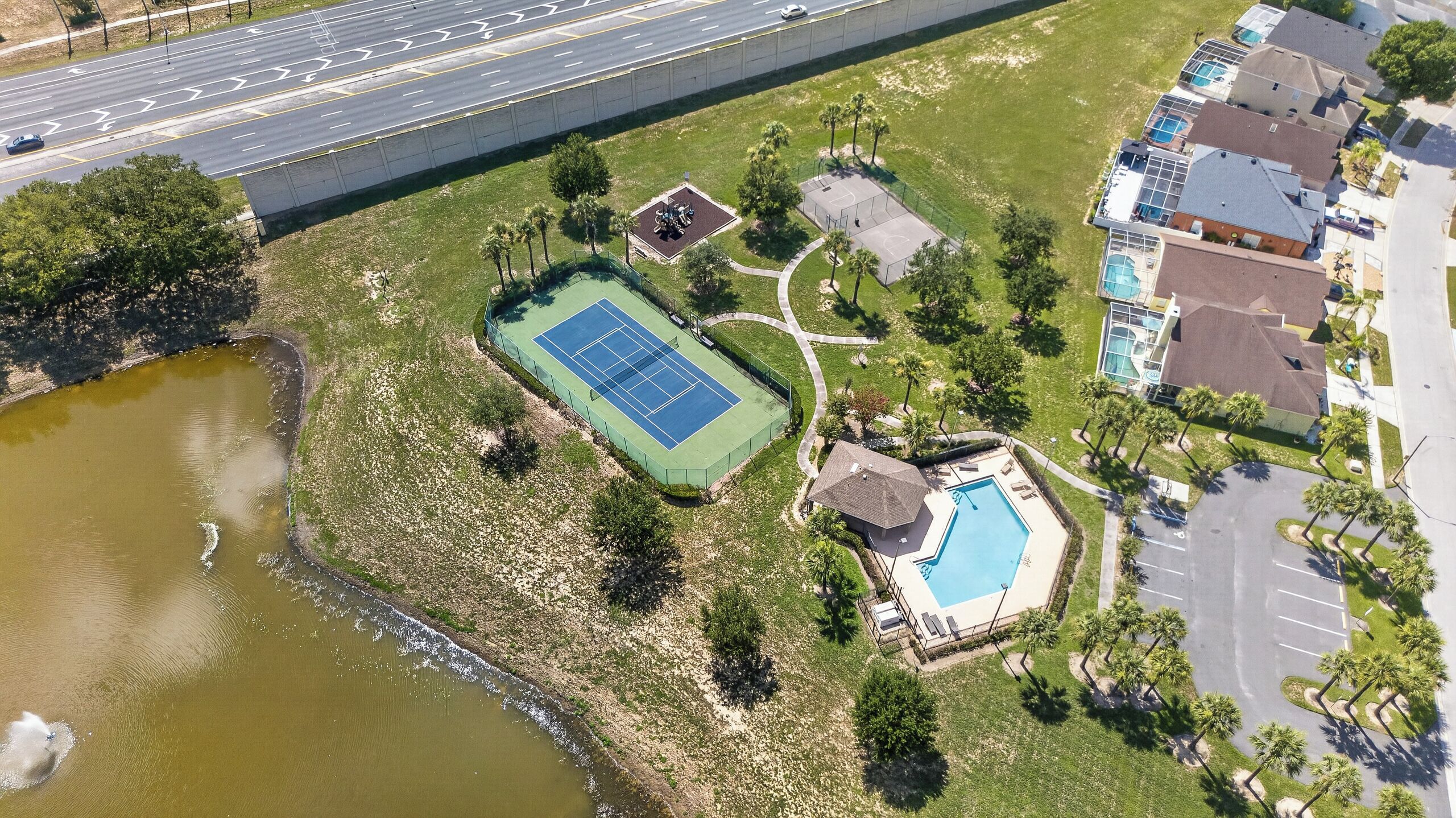 An aerial view of a property with a tennis court, a swimming pool, and a parking area.