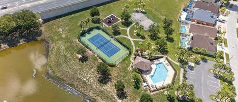 An aerial view of a property with a tennis court, a swimming pool, and a parking area.