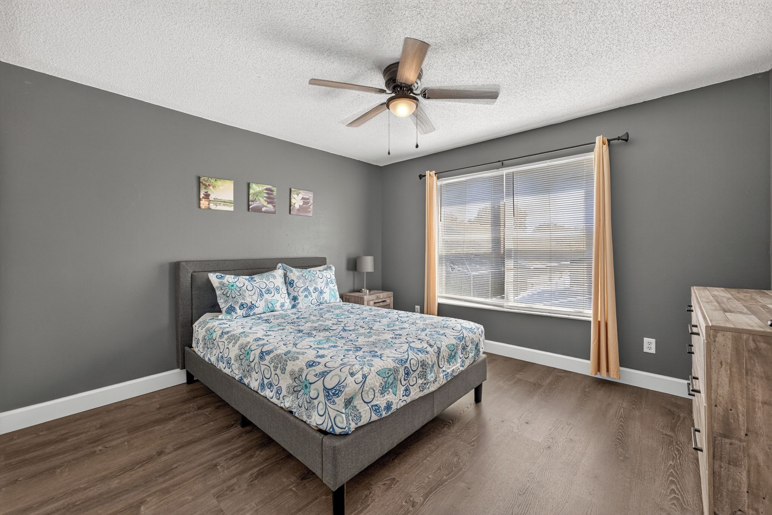A bedroom with a bed, a ceiling fan, a window with blinds, and a nightstand.