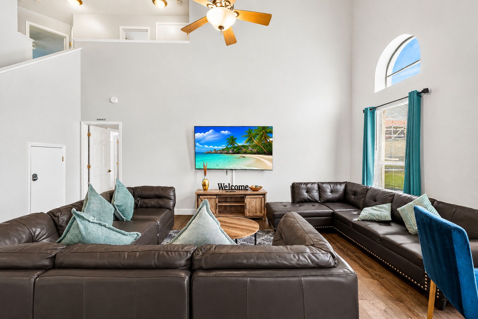 A modern living room with a sectional sofa, a flat-screen TV, and a ceiling fan.