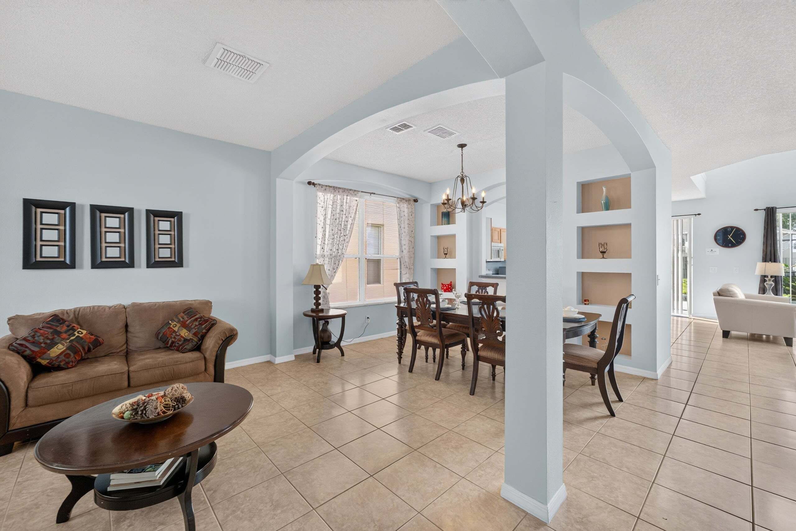 A spacious living room with a sofa, coffee table, and dining area with chairs and a chandelier.