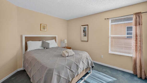 A bedroom with a bed, two bedside tables, a window with blinds, and a wall-mounted picture. - Emerald Magic Retreat - Minutes to Disney! Emerald Island Pool Home Retreat (Kissimmee)