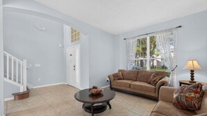 A living room with a sofa, coffee table, and a lamp. There is a staircase and a door leading to another room. - Emerald Magic Retreat - Minutes to Disney! Emerald Island Pool Home Retreat (Kissimmee)