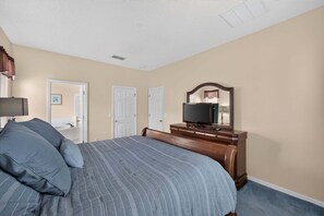 A bedroom with a bed, dresser, television, and two doors. - Emerald Magic Retreat - Minutes to Disney! Emerald Island Pool Home Retreat (Kissimmee)