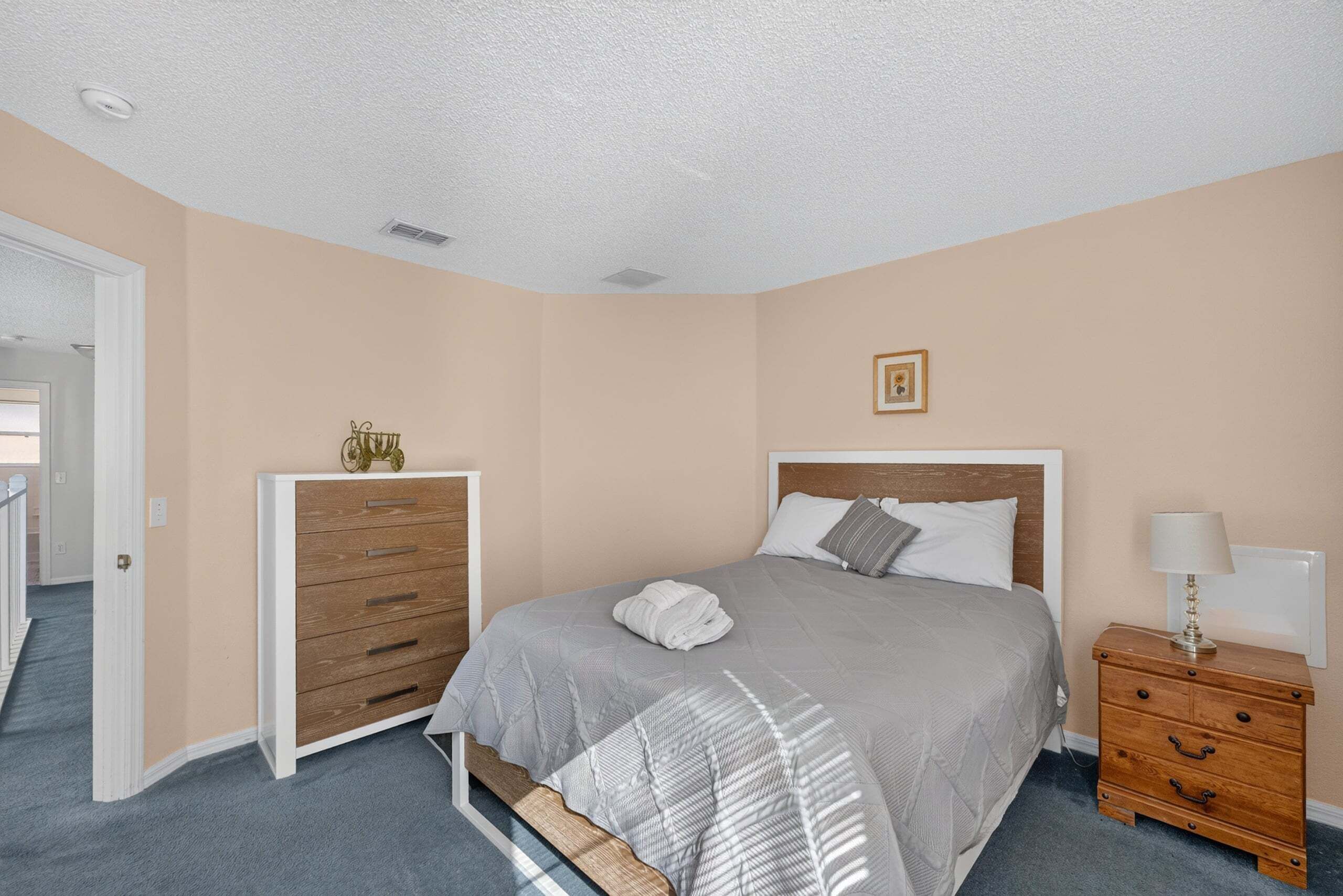 Um quarto com cama, cômoda, mesa de cabeceira e uma porta que dá para outro ambiente.