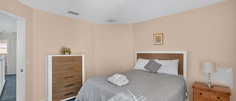 Um quarto com cama, cômoda, mesa de cabeceira e uma porta que dá para outro ambiente.