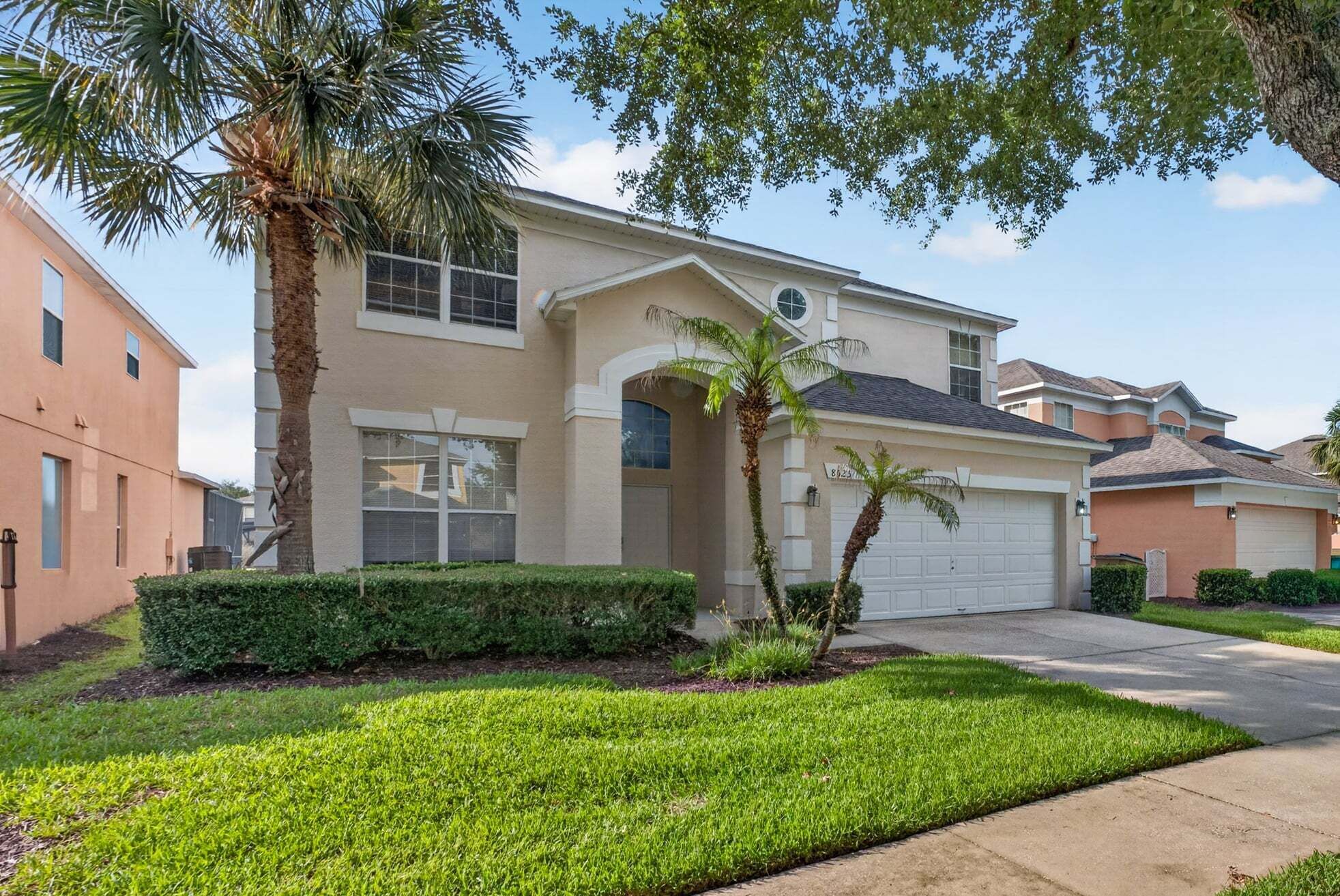 A two-story residential house with a garage, a well-maintained lawn, and a palm tree.