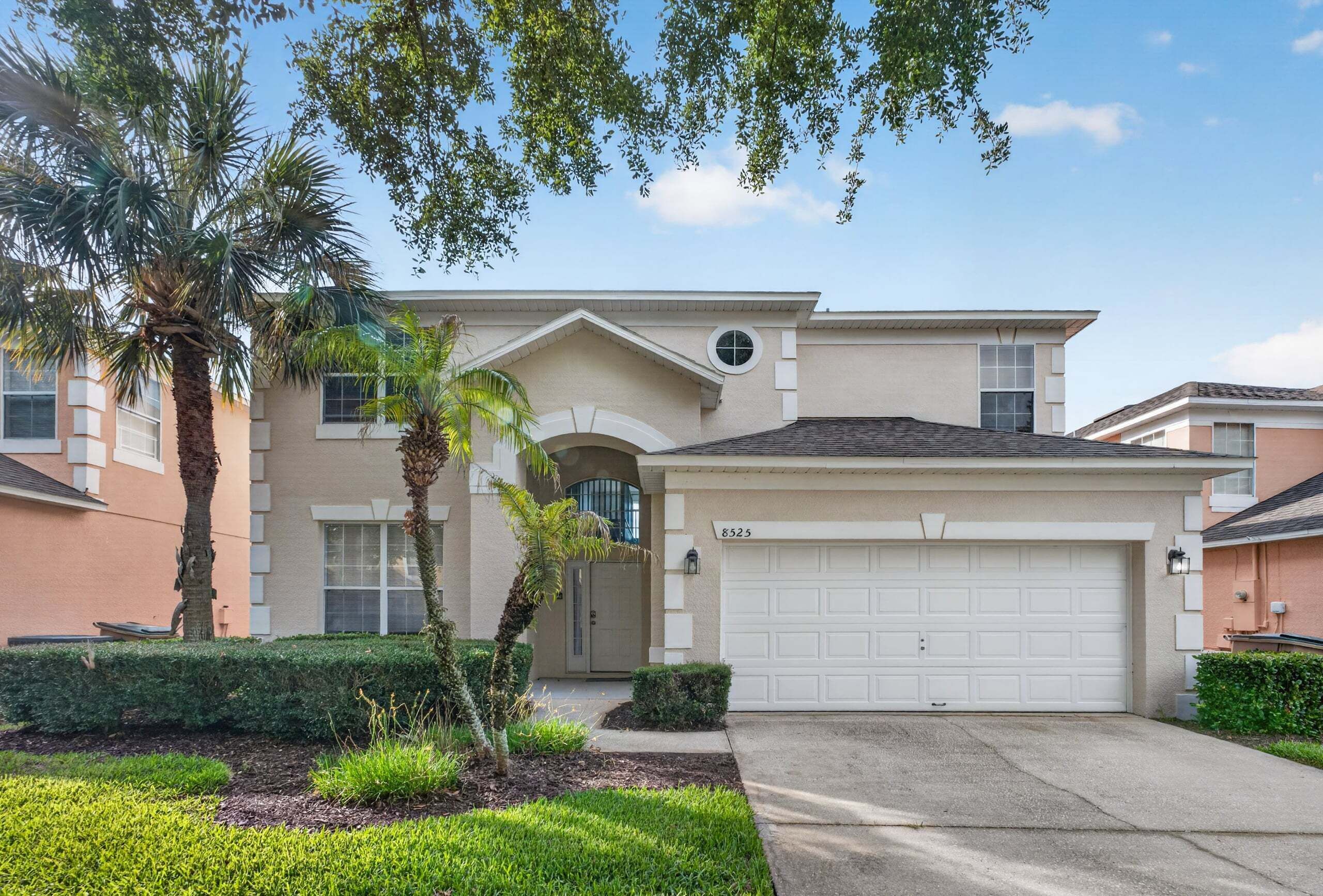 A residential building with a garage, a small porch, and a palm tree.