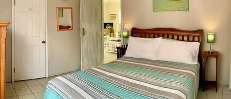 A hotel room with a bed, a door, a painting, and a view of the sea.