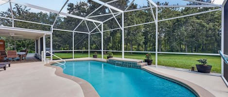 A swimming pool with a glass enclosure, surrounded by a patio area with outdoor furniture.
