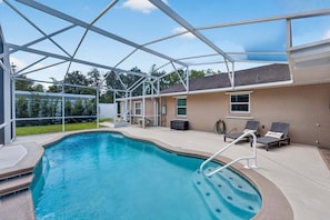 A covered outdoor swimming pool with a clear sky, a house in the background, and a patio area with lounge chairs. - Kis105-2601-4-pg - Shingle Creek Poolside Retreat (Kissimmee)