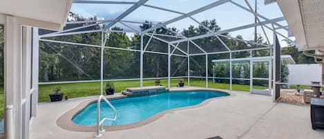 A covered outdoor swimming pool with a glass enclosure, surrounded by a patio area with seating and potted plants.