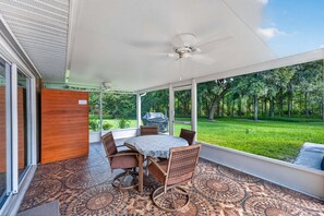 Eine überdachte Terrasse mit Tisch, Stühlen, großen Fenstern und einem Deckenventilator.