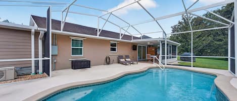 A swimming pool with a covered patio area, a house, and a lawn.