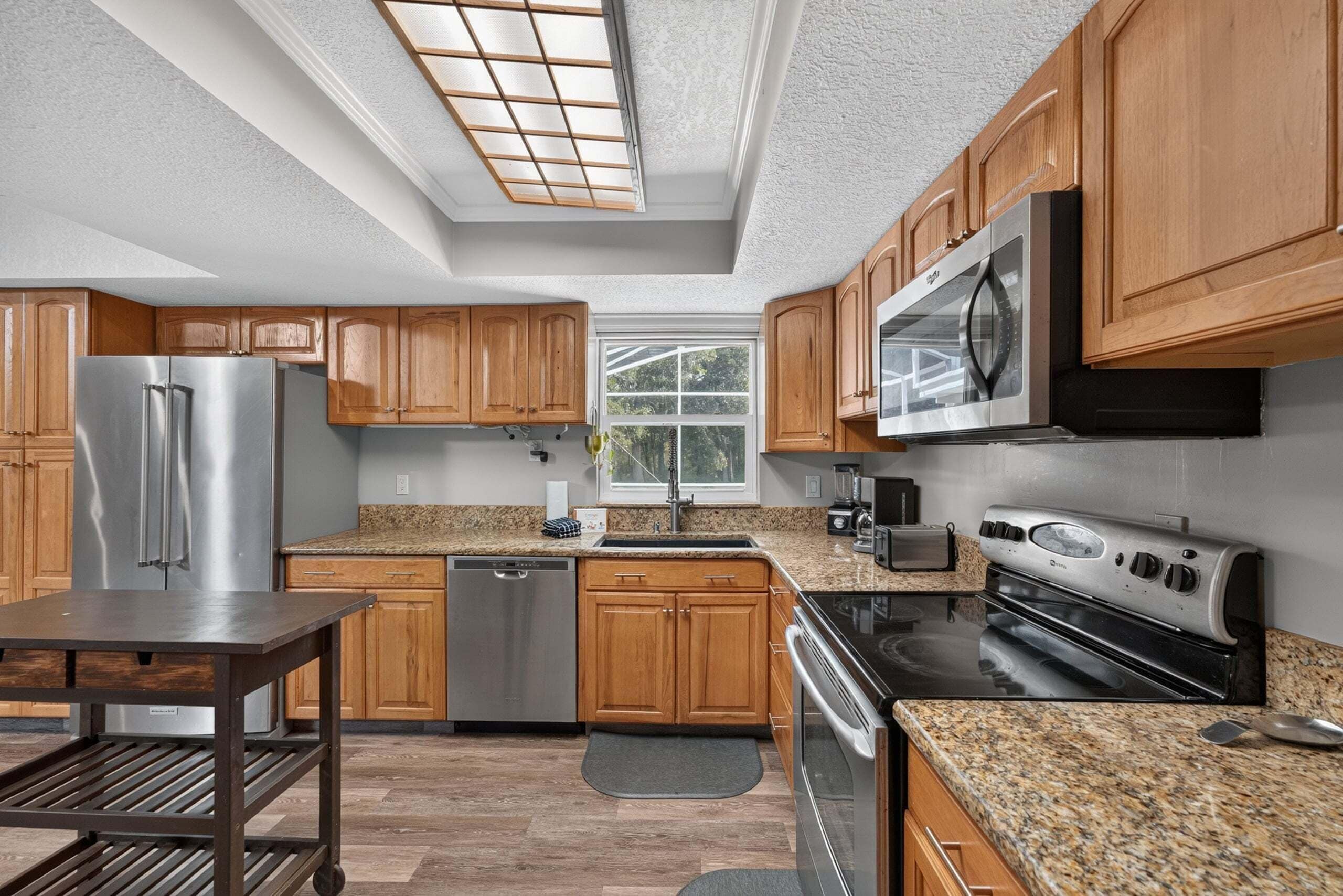 A modern kitchen with wooden cabinets, stainless steel appliances, and a large window.