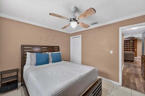 Ein Schlafzimmer mit einem Bett, einem Deckenventilator, einem Nachttisch und einer Tür zu einem anderen Raum.
