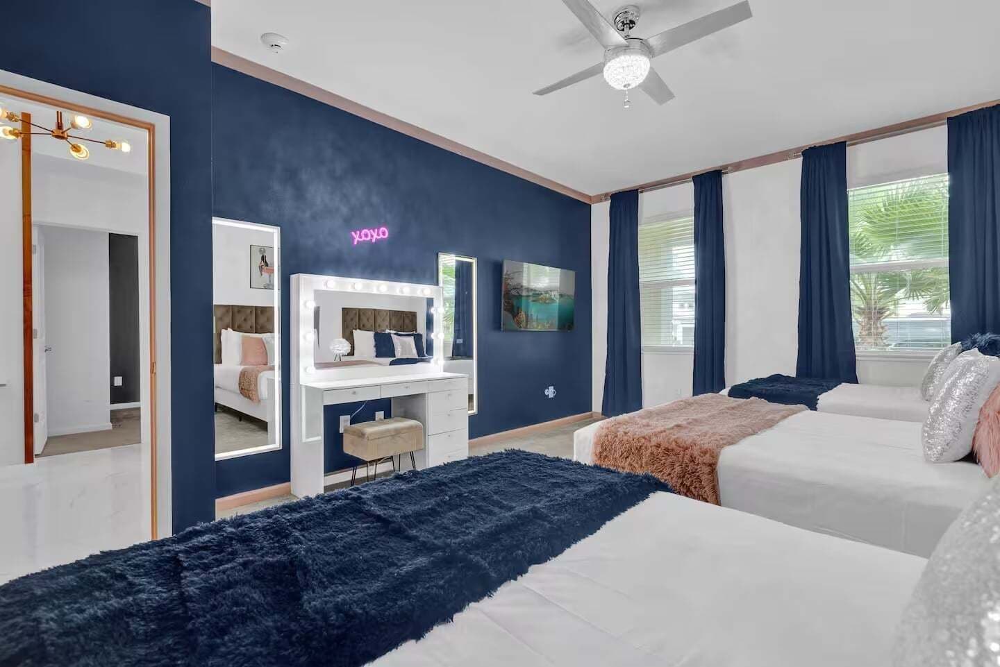 Een hotelkamer met een kaptafel, een bed, een bureau met spiegel en een plafondventilator.