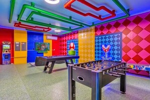 Ein hell erleuchteter Innenraum mit einem Kicker, einer Dartscheibe und einer farbenfrohen Wand mit Rautenmuster.