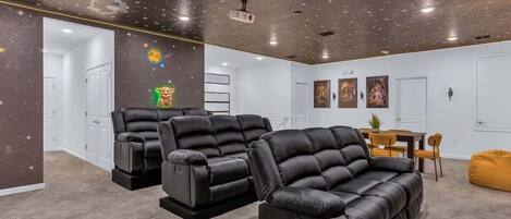 Ein Zimmer mit Sternenhimmel, einem schwarzen Ledersofa, einem gelben Sitzsack und einer Essecke mit Tisch und Stühlen.