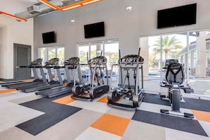 Ein Fitnessstudio mit Laufbändern, Crosstrainern und Fahrrädern, große Fenster und Blick ins Freie.