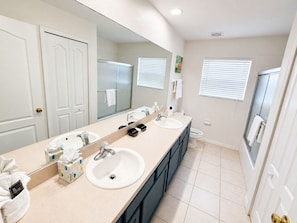 A modern bathroom with two sinks, a large mirror, and a shower. - King's Way Haven - 7BR Golf-view Home With Pool and Game Room (Davenport)