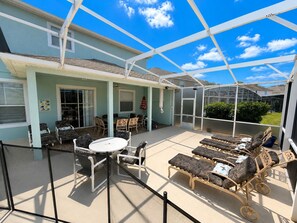 A covered patio area with outdoor furniture, a table, and a greenhouse structure. - King's Way Haven - 7BR Golf-view Home With Pool and Game Room (Davenport)