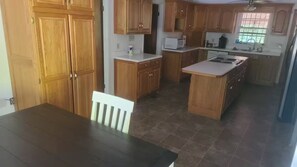 A kitchen with wooden cabinets, a white countertop, and a dining table with a white chair.