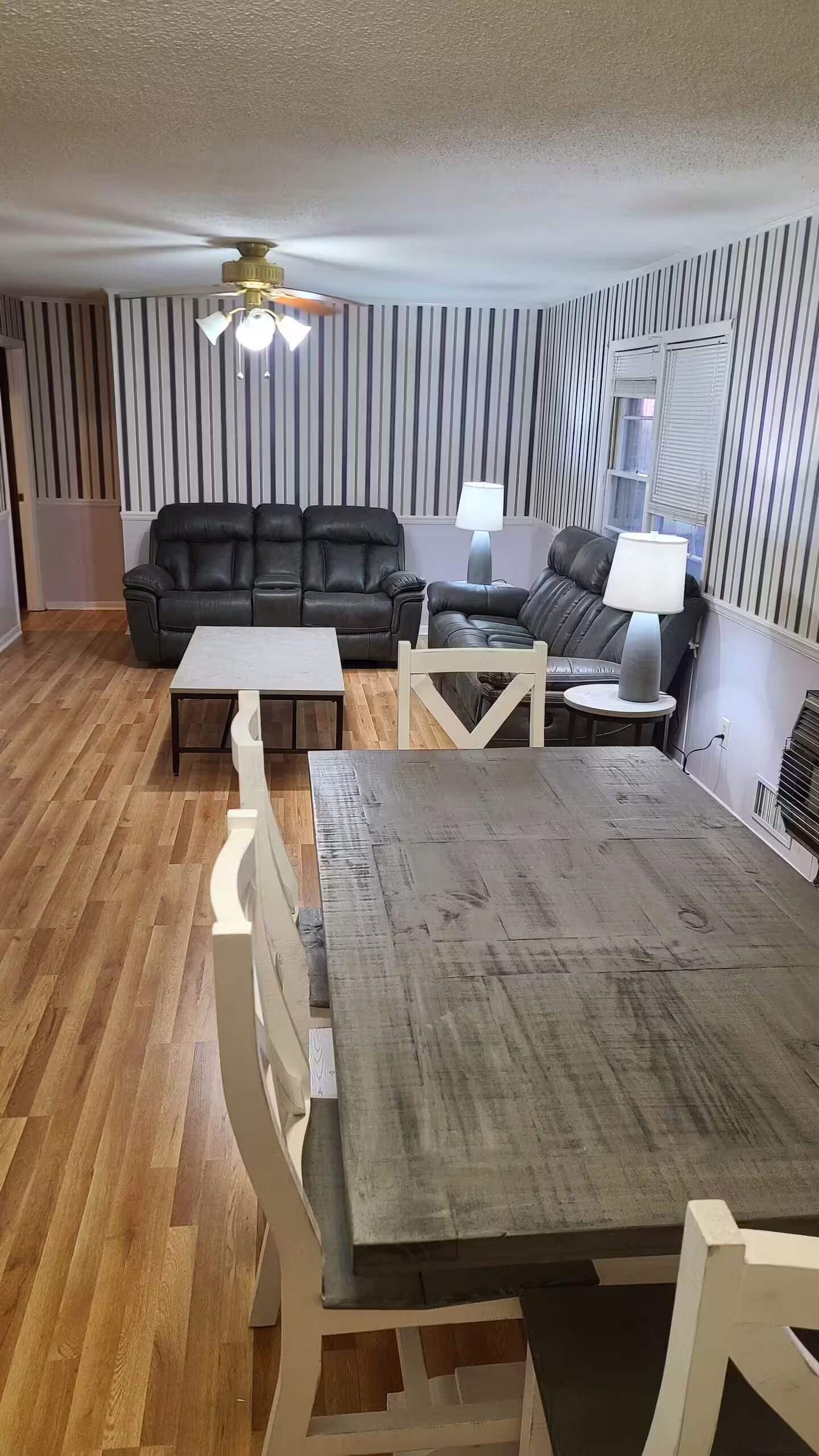 Een woonkamer met een bank, twee fauteuils, een salontafel en een eettafel.