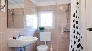 A bathroom with a sink, toilet, shower, and a window.
