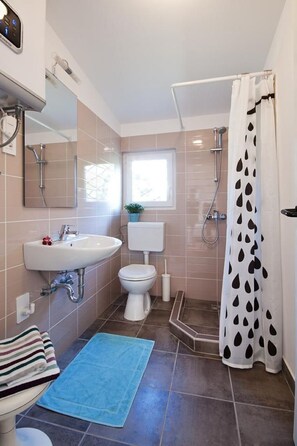 A bathroom with a sink, toilet, shower, and a window.